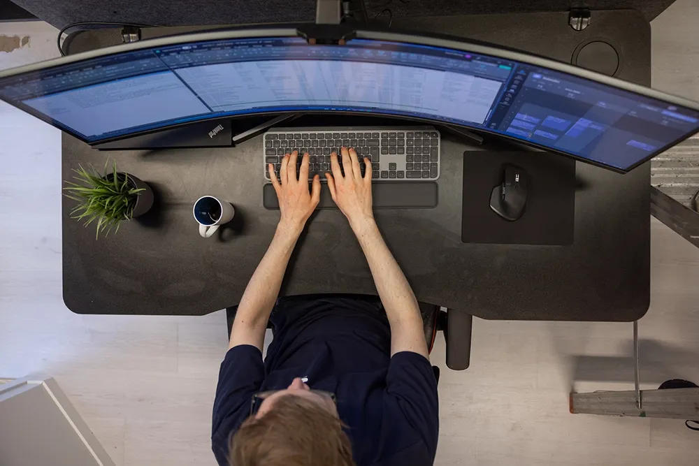 Bilde tatt ovenfra og ned med en person som jobber foran skjerm - Nettvakt