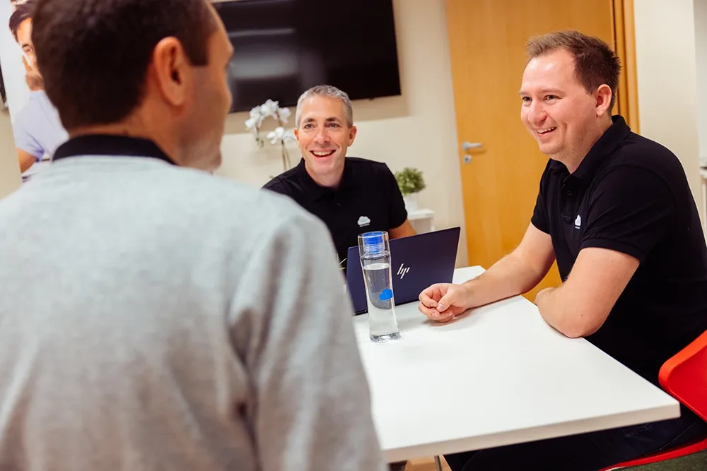 3 personer smilende rundt et møtebord - Microsoft Teams