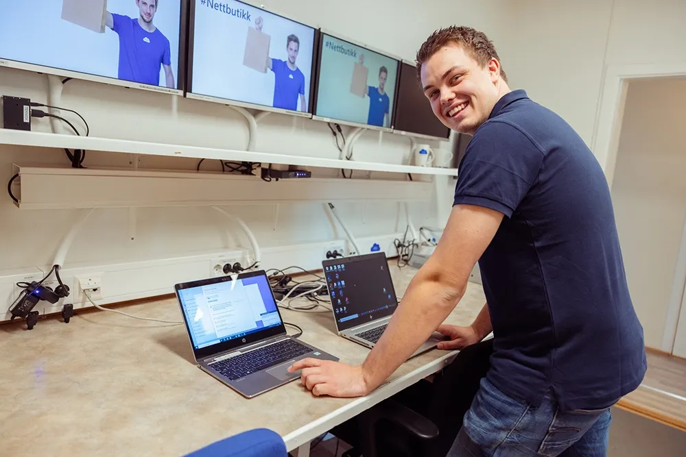 En tekniker smiler mot kamera mens han jobber på testbenken med migrering